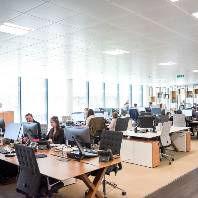 Modernes Büro mit arbeitenden Angestellten an Schreibtischen und Computern, natürliches Licht durch große Fenster